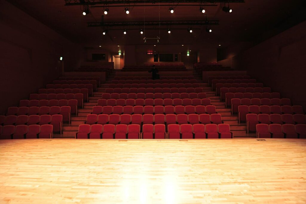An empty theater interior with rows of red seats and an illuminated stage.