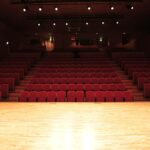 An empty theater interior with rows of red seats and an illuminated stage.